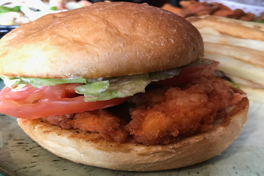 Plate with a fried chicken sandwich and fries on it, along with a bowl of food items in the background