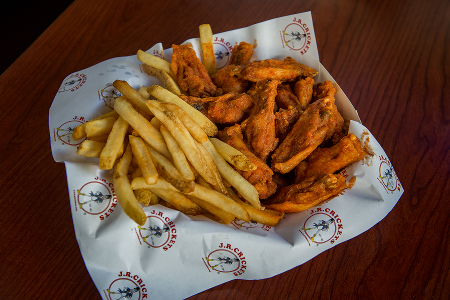 Basket filled with golden-brown fried chicken wings and french fries on top of a wooden table